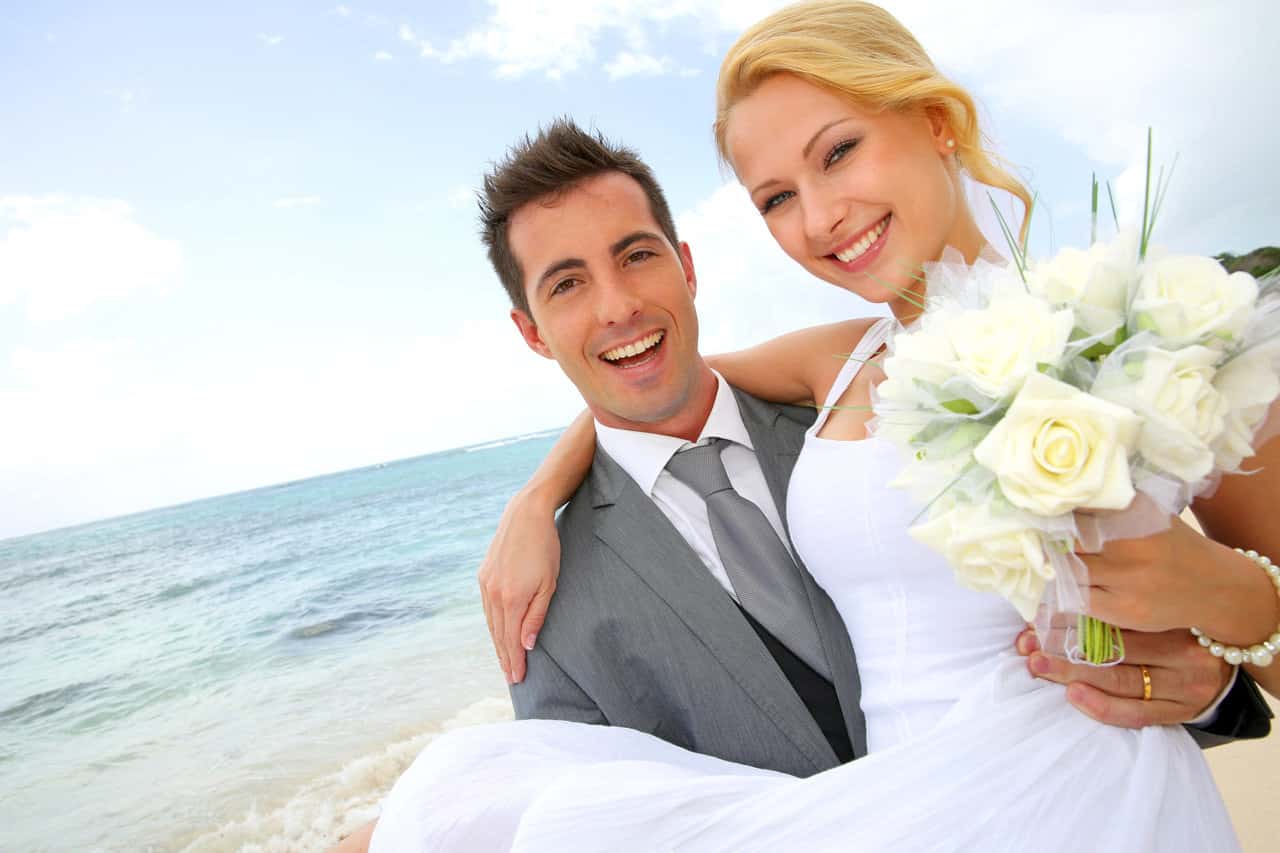 Bräutigam trägt seine Braut auf Händen am Strand